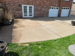 This is an exposed aggregate patio and driveway.  It is not supposed to be light in color.  Rather than looking decorative as intended, it looks like plain concrete with rocks in it.